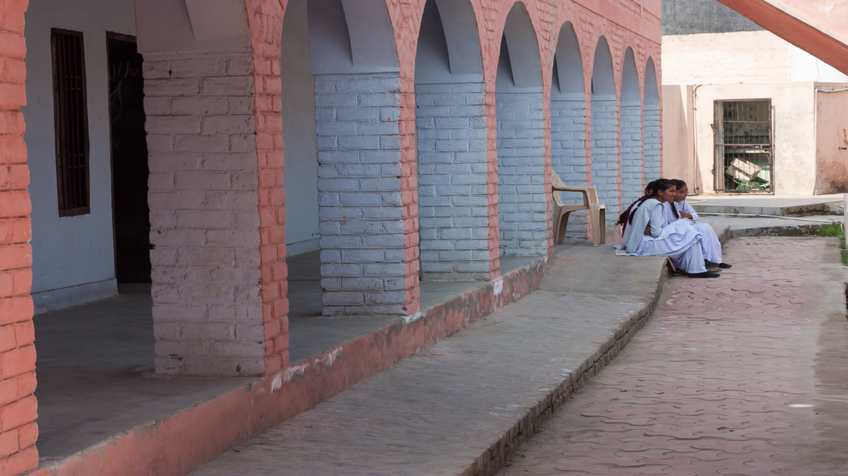Three adolescent girls sitting outside their school corridor